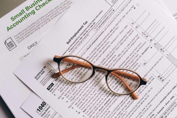 Overhead view of tax documents and eyeglasses on a laptop keyboard, ideal for finance or accounting themes.